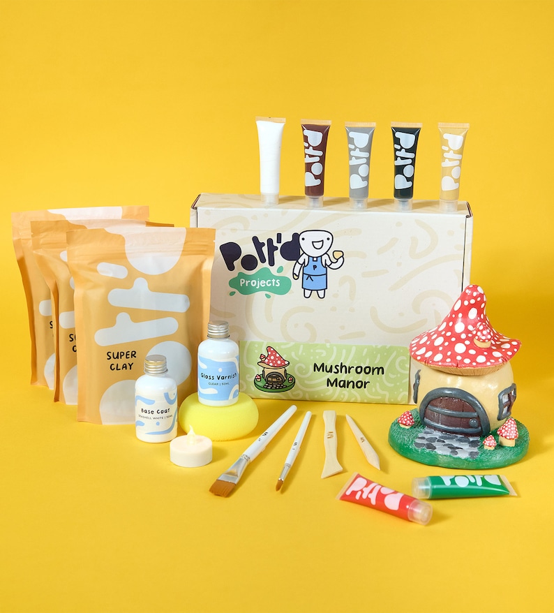 May include: A mushroom-shaped house craft kit with a box of white, brown, gray, black, and gold paint, a box of clay, a bottle of gloss varnish, a bottle of base coat, a sponge, a candle, and five tools. The box has the text "Potty's Projects" and "Mushroom Manor".