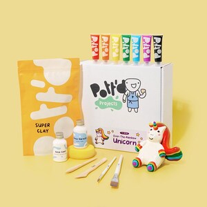 K&ouml;nnte beinhalten: Ein Bastelset zum Herstellen einer Einhornfigur. Das Set enth&auml;lt wei&szlig;en Ton, Farbe, Pinsel und Werkzeuge. Die Schachtel tr&auml;gt den Text "Over-The-Rainbow Unicorn".
