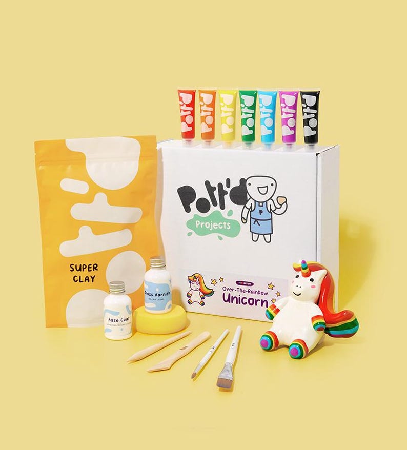 K&ouml;nnte beinhalten: Ein Bastelset zum Herstellen einer Einhornfigur. Das Set enth&auml;lt wei&szlig;en Ton, Farbe, Pinsel und Werkzeuge. Die Schachtel tr&auml;gt den Text "Over-The-Rainbow Unicorn".