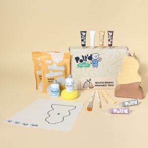 May include: A pottery kit for making a vase. The kit includes clay, paint, brushes, and a template. The vase is a minimalist design with a light brown and yellow color scheme. The box says "Blissful Blooms Minimalist Vase".