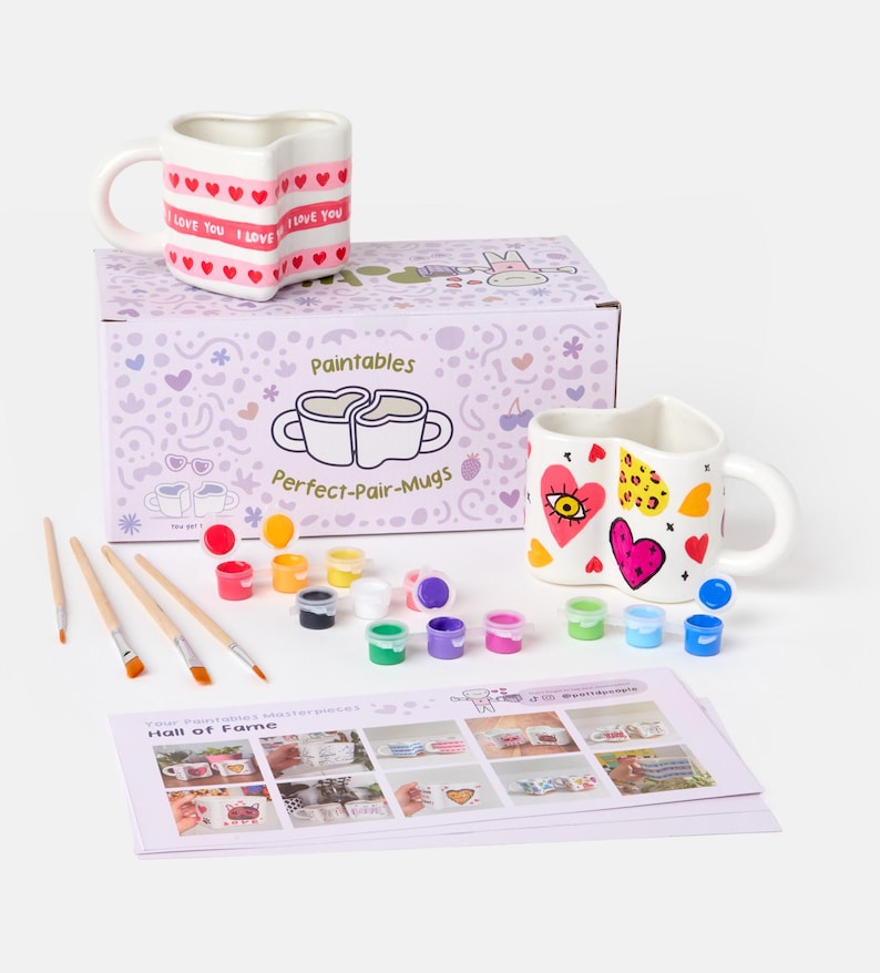 Puede incluir: Un kit de tazas para pintar con dos tazas en forma de coraz&oacute;n, botes de pintura y pinceles. Una taza tiene el texto "I LOVE YOU" y corazones. La otra taza tiene un dise&ntilde;o de coraz&oacute;n y ojo. El kit incluye una caja con el texto "Perfect-Pair-Mugs".
