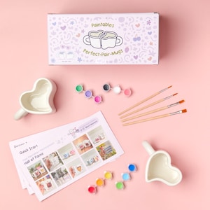 Puede incluir: Un kit de tazas para pintar con tazas en forma de coraz&oacute;n, botes de pintura y pinceles. El kit incluye una caja con el texto "Paintables Perfect-Pair-Mugs". Tambi&eacute;n se incluye una gu&iacute;a con im&aacute;genes de tazas pintadas.