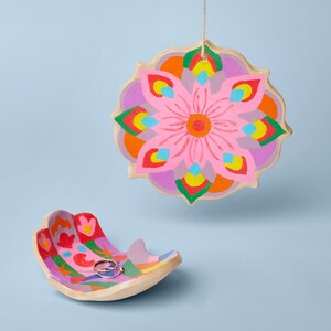 K&ouml;nnte beinhalten: Eine farbenfrohe Keramikschale mit einem rosafarbenen Blumendesign und einem Ring darin. Die Schale ist handf&ouml;rmig und hat ein helles, mehrfarbiges Muster.