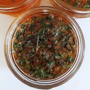 May include: A glass jar filled with a clear amber liquid and green herbs. The jar is sitting on a white surface.
