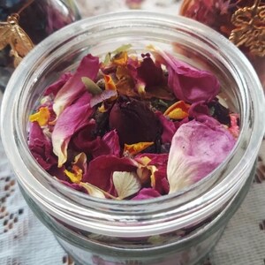 May include: A glass jar filled with dried rose petals, including pink, red, and white petals. The petals are mixed with other dried flowers and herbs.