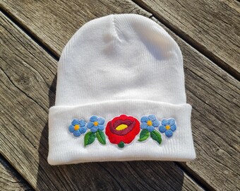 Puede incluir: Gorro de punto blanco con una flor roja y flores azules bordadas en el borde.