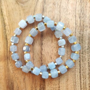 May include: Two bracelets made of light blue square beads with silver and gold accents.