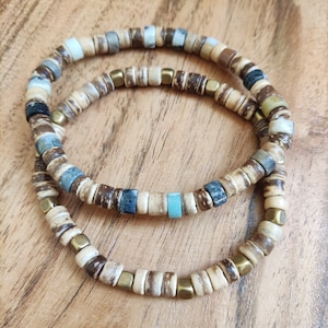 Op de afbeelding: Twee armbanden gemaakt van bruine houten kralen met gouden accenten. Een armband heeft een turquoise kraal.