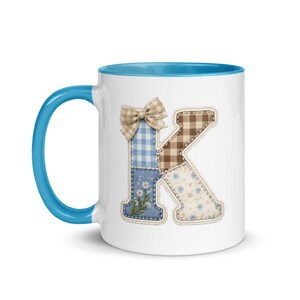 Può includere: Tazza in ceramica bianca con interno e manico blu. La tazza presenta un design patchwork della lettera "K" con fiocco, quadretti, motivi floreali e tinta unita in blu, marrone e bianco. Un oggetto affascinante e decorativo.