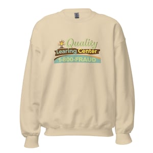 以下が含まれることがあります： クリーム色のスウェットシャツ。緑と茶色で「Quality Learning Center」の文字、青色で電話番号「1-800-FRAUD」がプリントされています。クルーネックと長袖のデザインです。