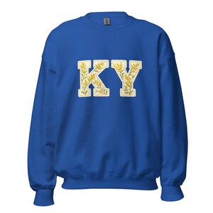 Peut inclure: Sweat-shirt bleu roi avec les lettres "KY" en blanc, dans une police de style universitaire. Les lettres sont remplies d'un motif floral jaune. Le sweat-shirt a des manches longues et un col rond.