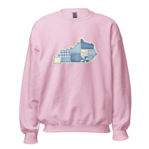 Peut inclure: Un sweat-shirt rose clair orné d'un motif patchwork représentant l'État du Kentucky. Le contour du Kentucky est rempli de divers tissus bleus et blancs à motifs, notamment du vichy, des pois et des textures semblables au denim. Le sweat-shirt a un col rond et des manches longues.