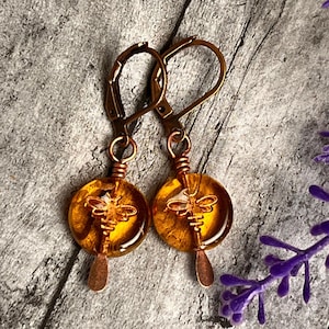 May include: A pair of gold tone earrings with amber glass beads featuring a bee design. The beads are round and have a textured surface.