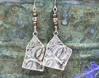 May include: Silver dangle earrings with a geometric design and brown beads. The earrings have a textured, ornate look.