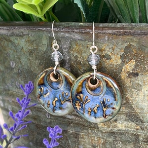 May include: A pair of blue and brown ceramic earrings with silver hooks and clear glass beads. The earrings feature a floral design.
