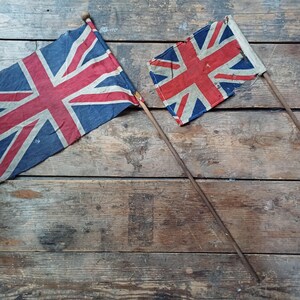 May include: Two Union Jack flags on wooden poles. The flags display the red, white, and blue cross design. They are set against a backdrop of aged, wooden planks.
