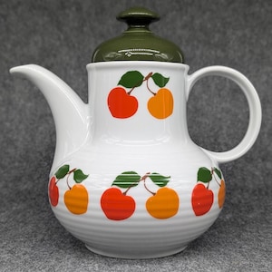 Könnte beinhalten: Weiße Keramik-Teekanne mit grünem Deckel und Kirschendesign. Die Teekanne hat einen runden Korpus mit einem breiten Ausguss und einem Henkel. Die Kirschen sind rot und orange mit grünen Blättern.
