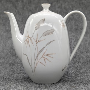 Könnte beinhalten: Weiße Keramik-Teekanne mit einem Blumendesign mit braunen und grauen stilisierten Weizenähren. Die Teekanne hat einen Deckel und einen Henkel.