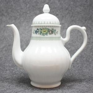 Könnte beinhalten: Weiße Porzellan-Kaffeekanne mit Deckel und floralem Design in Grün, Gelb und Blau.