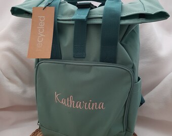 Könnte beinhalten: Ein blaugrüner Rucksack mit Rollverschluss und verstellbaren Trägern. Der Rucksack hat ein kleines Etikett mit der Aufschrift "recycled" und ist mit dem Namen "Katharina" bestickt.