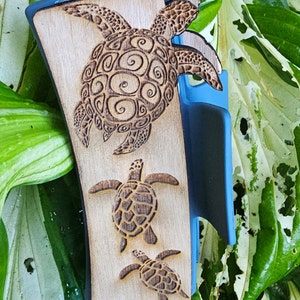May include: A wooden phone case with a blue edge, featuring a carved design of three sea turtles. The turtles are intricately detailed with swirling patterns.