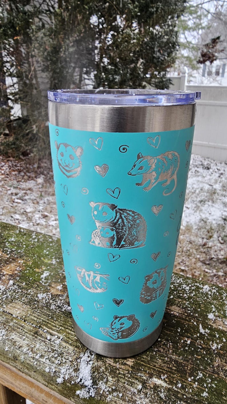 May include: A turquoise stainless steel tumbler with a silver design of opossums and hearts.