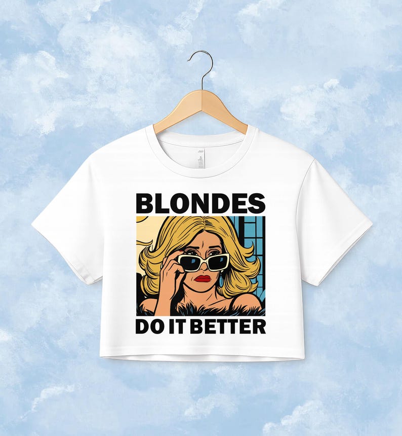 Pu&ograve; includere: Una t-shirt corta bianca con un'illustrazione grafica di una persona bionda che indossa occhiali da sole. Il testo BLONDES DO IT BETTER &egrave; stampato in lettere maiuscole nere sopra e sotto l'illustrazione in stile fumetto.