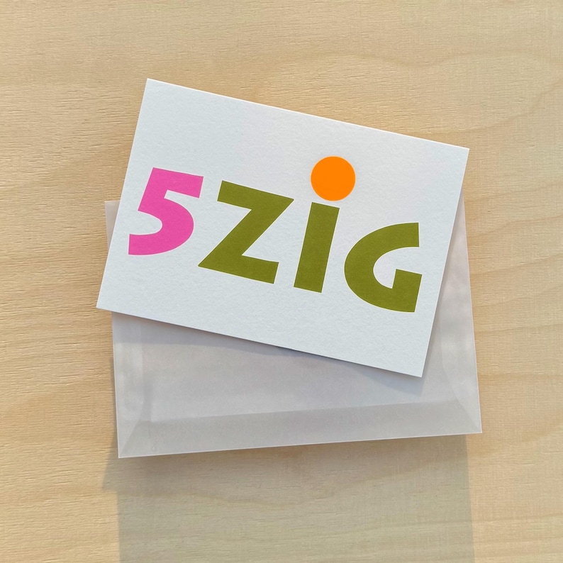 May include: A white card with the text "5zig" in green and pink letters. A small orange circle is above the "g".