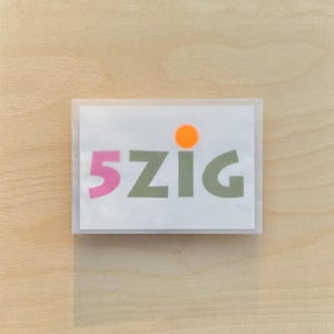 May include: A white card with the text "5ZIG" in pink and green letters. A small orange circle is above the text.