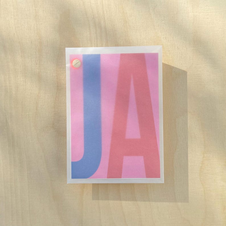 May include: A pink card with the letters "JA" printed in blue and pink.