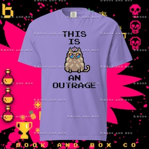 May include: A light purple t-shirt with the text "THIS IS AN OUTRAGE" and a pixelated cat wearing sunglasses and a crown. The shirt is a short-sleeved crew neck.