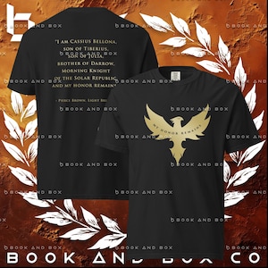 May include: Black t-shirts with gold text and graphics. One shirt features a phoenix design with "MY HONOR REMAINS". The other shirt has text from Pierce Brown's "Light Bringer" book.