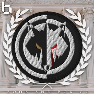 Pode incluir: Etiqueta bordada em preto e branco com um design estilizado de cabeça de lobo. A cabeça do lobo é dividida ao meio, um lado preto e o outro branco. O lobo tem um olho vermelho e uma lágrima vermelha escorrendo pelo rosto.