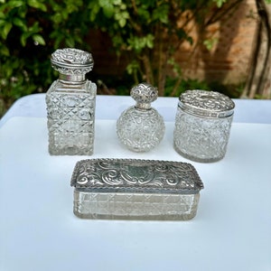 May include: A set of four vintage glass bottles with silver lids. The bottles are clear and have a textured surface. The lids are ornate and have a silver finish.