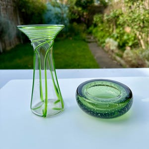 May include: Two green glass vases. One vase is tall and slender with a clear body and green lines. The other vase is short and round with a green body and small air bubbles.
