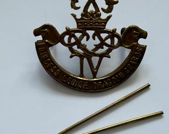 May include: A gold-colored metal badge with a crown and the words "Princess Louise Dragoon Guards" around the edge.