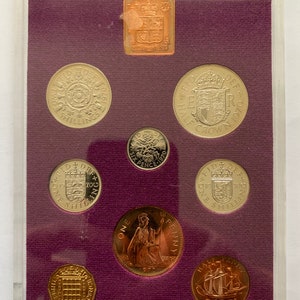 Op de afbeelding: Een set van acht Britse munten uit 1970 in een doorzichtige plastic doos met een paarse fluwelen achtergrond. De munten omvatten een halve penny, een penny, een twee pence, een vijf pence, een tien pence, een shilling, een halve kroon en een kroon.