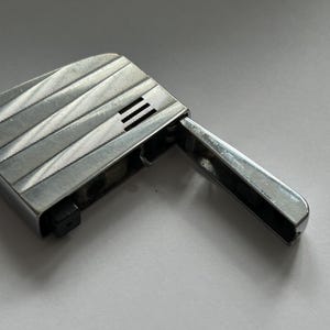 May include: A silver lighter with a textured design and a flip-top lid. The lighter is open and the flint wheel is visible.