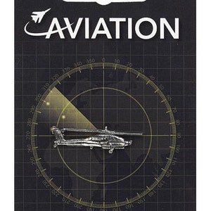 May include: A silver pin badge featuring a helicopter silhouette against a black and white radar screen background. The text "AVIATION" is printed in white above the image and "PIN BADGE" is printed in white below the image.