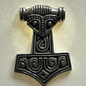 Könnte beinhalten: Ein silberfarbener Anhänger in Form von Thors Hammer, Mjolnir, mit filigranen Details und einem Knotendesign.
