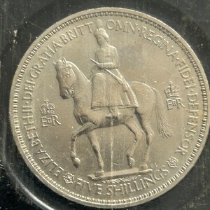 Puede incluir: Moneda de plata con un perfil de la reina Isabel II a caballo con la inscripción "ELIZABETH II DEI GRATIA BRIT. OMN. REGINA F.D. DEFENSOR", y la denominación "FIVE SHILLINGS" en la parte inferior.