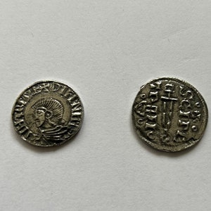 May include: Two silver coins with raised lettering and images. One coin features a profile of a person wearing a crown and the other coin features a sword.