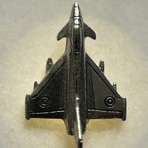 Puede incluir: Un modelo de avión de combate de metal plateado. El avión tiene una nariz puntiaguda y alas en flecha. El modelo está detallado con marcas redondas en las alas.