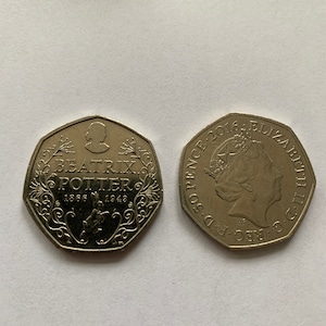 May include: A gold-coloured British 50 pence coin featuring a portrait of Queen Elizabeth II on one side and a design commemorating Beatrix Potter on the other side. The coin has the text "2016: ELIZABETH II D.G. REG. F.D. 50 PENCE" on the side with the Queen's portrait and "BEATRIX POTTER 1866 1943" on the other side.