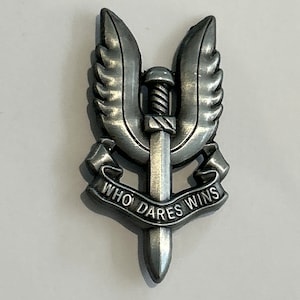 May include: A silver metal pin with a winged dagger and the text "WHO DARES WINS".
