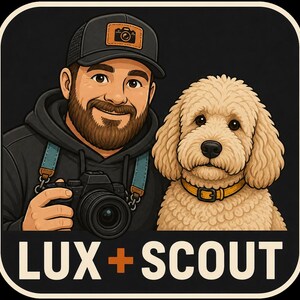 May include: A cartoon illustration featuring a bearded person wearing a black cap with a camera icon and a black hoodie, holding a black camera with a blue strap. Beside them is a fluffy tan dog with a yellow collar. The text LUX + SCOUT is below.