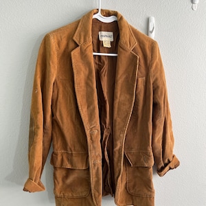 Puede incluir: Una chaqueta de pana marrón con un parche en el codo y la palabra "montera" en la etiqueta.