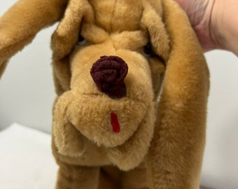 May include: A plush brown and tan dog toy with floppy ears and a red nose. The dog has a brown nose and a red mouth.