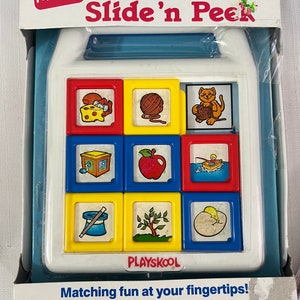 May include: A Playskool Slide 'n Peek toy with a blue and white frame. The toy has nine colorful sliding blocks with different images on each side. The images include a cat, a ball of yarn, a cheese wedge, a gift box, an apple, a fishing boat, a magic wand, a tree, and an egg. The toy is labeled "Playskool" and "Matching fun at your fingertips!" The box also includes a phone number for customer service: 1-800-PLAYSKL.