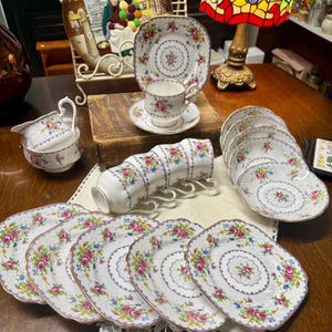 May include: A white ceramic mug with a black handle and the text "But First, Coffee" in a bold, black font. The mug is set against a blurred background, suggesting a cozy setting.